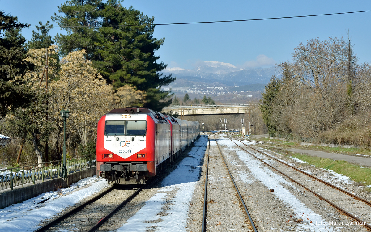 Ve stanici Bralos zastavuje vlak IC 53 (Soluň-Atény) vedený stroji  220.019 + 031. Krátce poté se vzájemně vymění lokomotivní čety s křižujícím IC 884 (Atény-Kalambaka).
